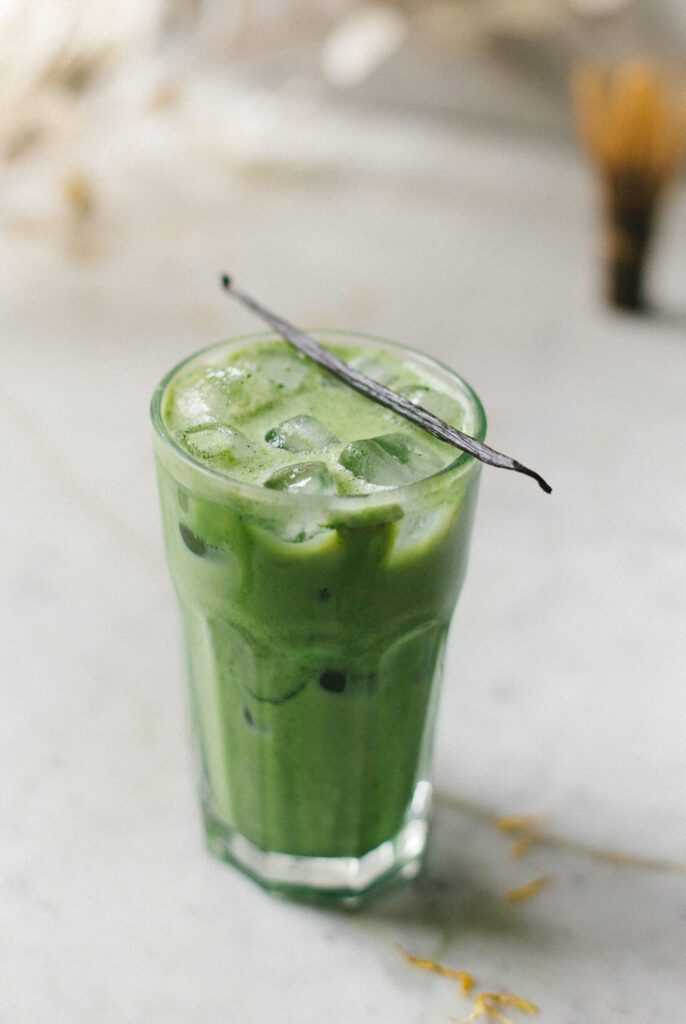 vanilla matcha latte klaar om te drinken met een vanille stokje op het glas als decoratie